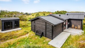 Eine moderne Hütte mit einer Terrasse und Sitzgelegenheiten im Freien, eingebettet in eine natürliche Landschaft.