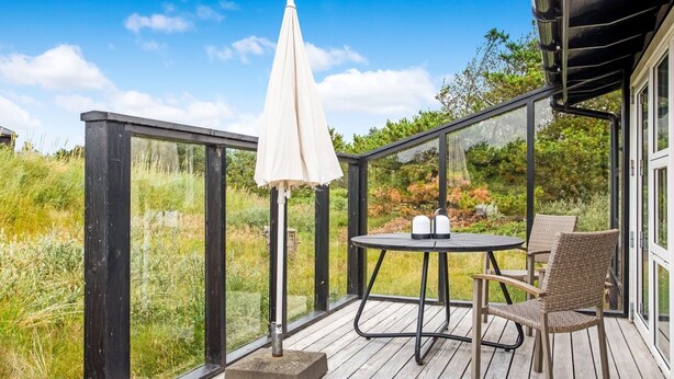Eine Terrasse mit Tisch und Stühlen, einem weißen Sonnenschirm und einer Glasveranda mit Blick auf eine Rasenfläche.
