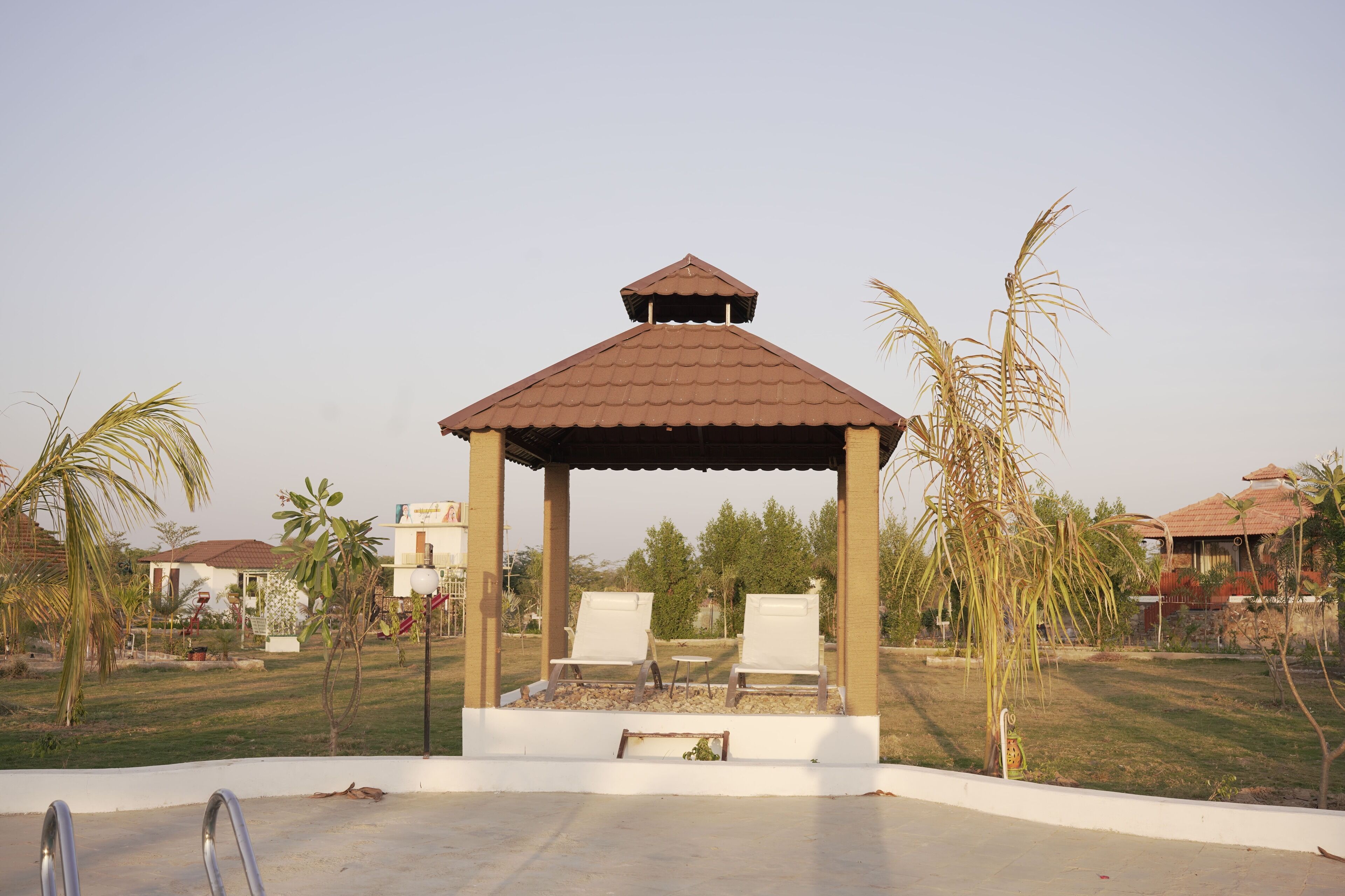 A gazebo with a tiled roof, two white lounge chairs, and a small table.
