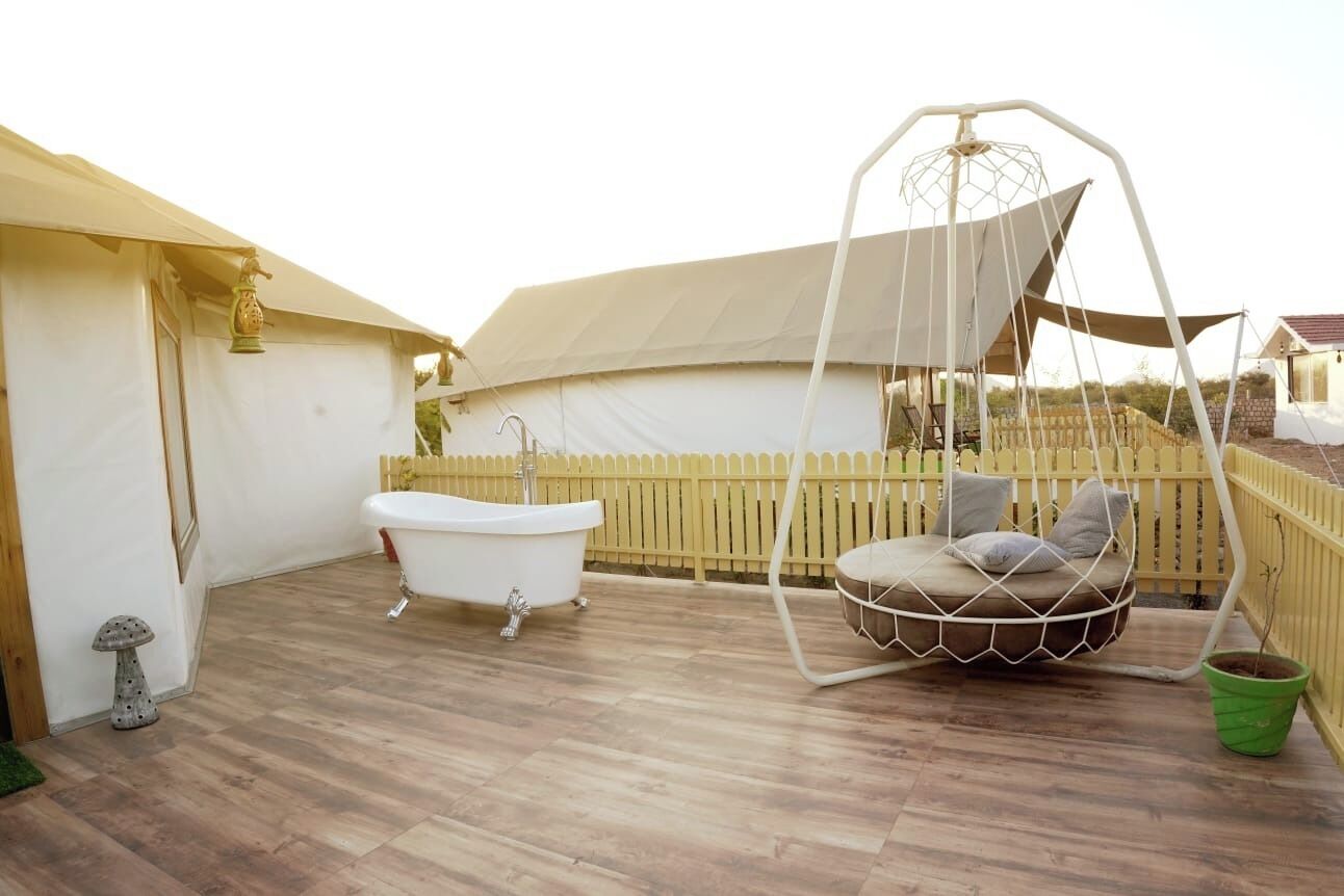 Una terraza de madera con una bañera blanca, una silla colgante tipo hamaca y una pequeña planta en maceta.