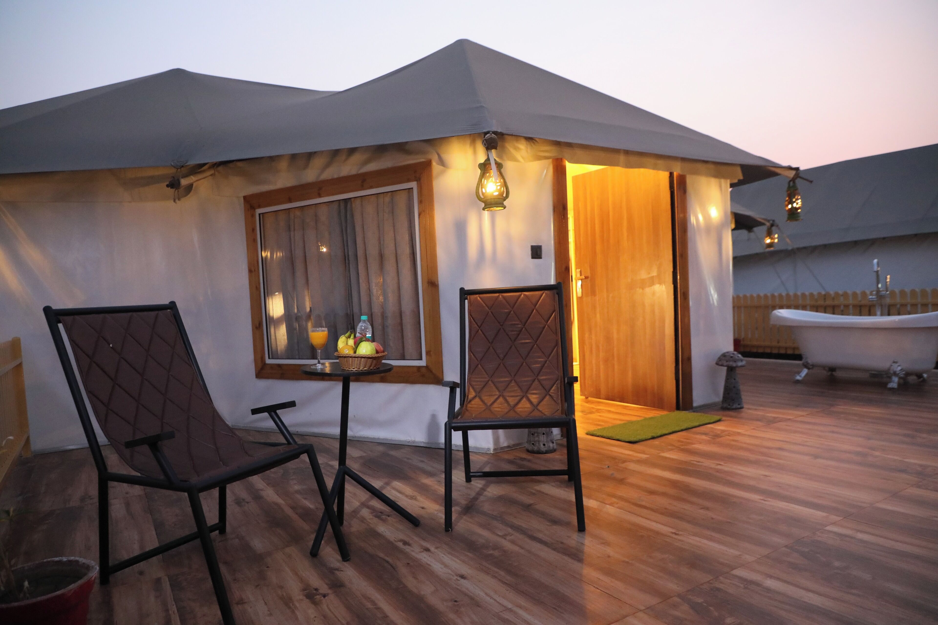Un espacio al aire libre con toldo, dos sillas, una mesa con fruta, una bañera y una terraza de madera.
