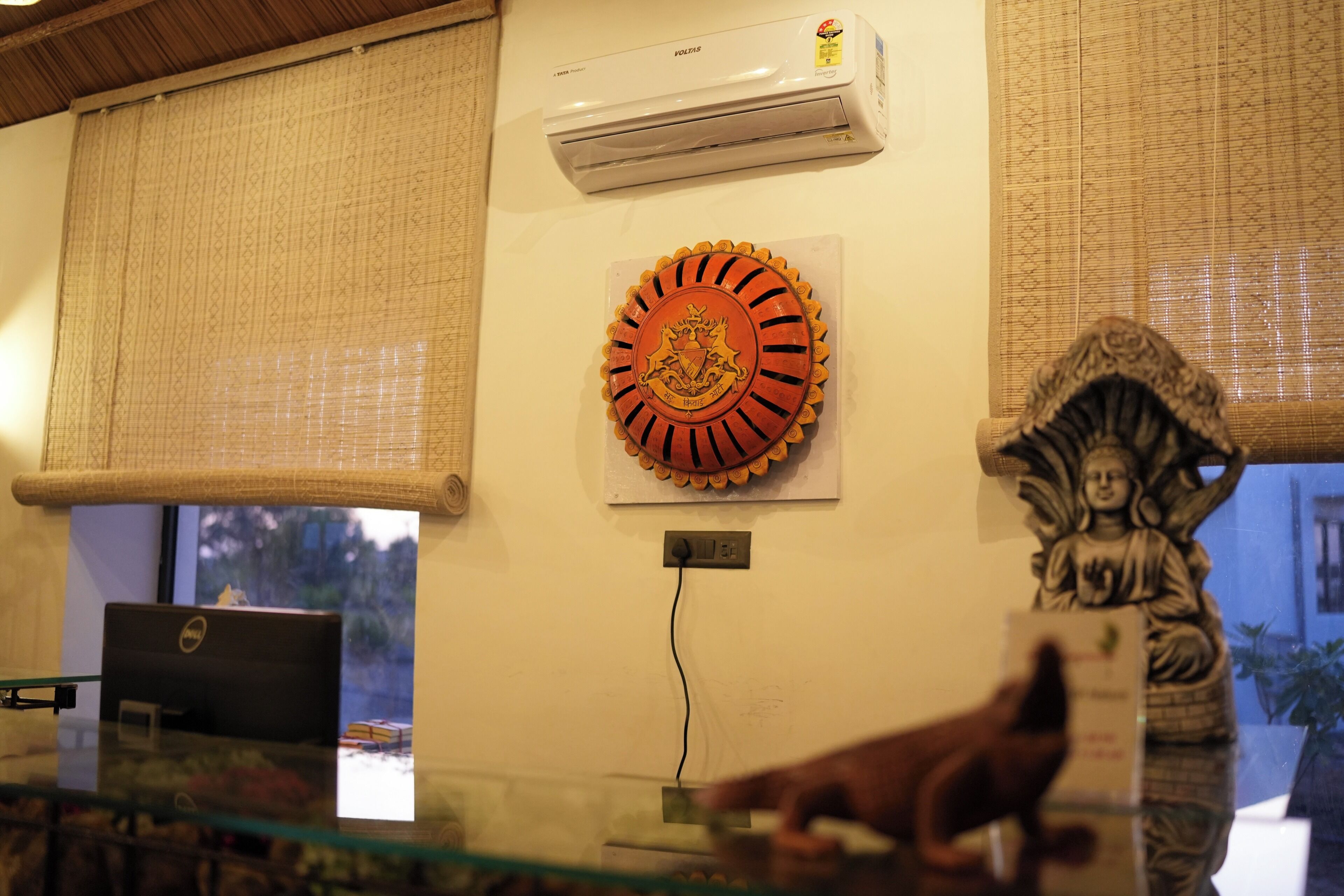 A room with a laptop on a glass table, a decorative plate on the wall, and a statue.