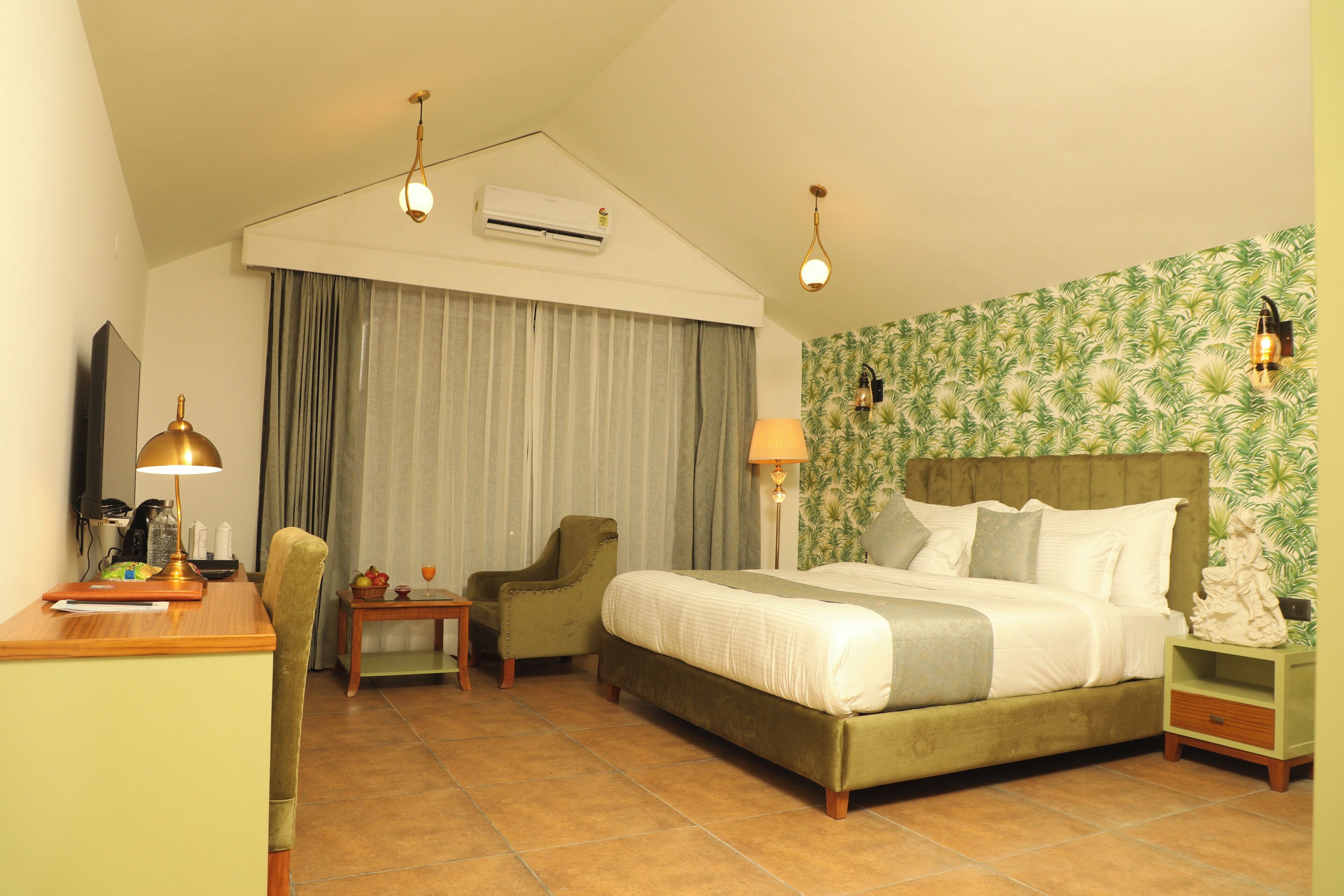 Une chambre d’hôtel comprenant un lit, un bureau, une chaise, une lampe et un mur recouvert d’un papier peint à motifs tropicaux.