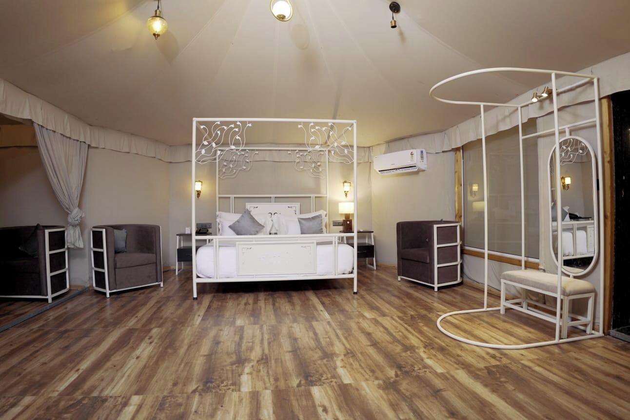 Un dormitorio con cama blanca, dosel, tocador con espejo y suelo de madera.