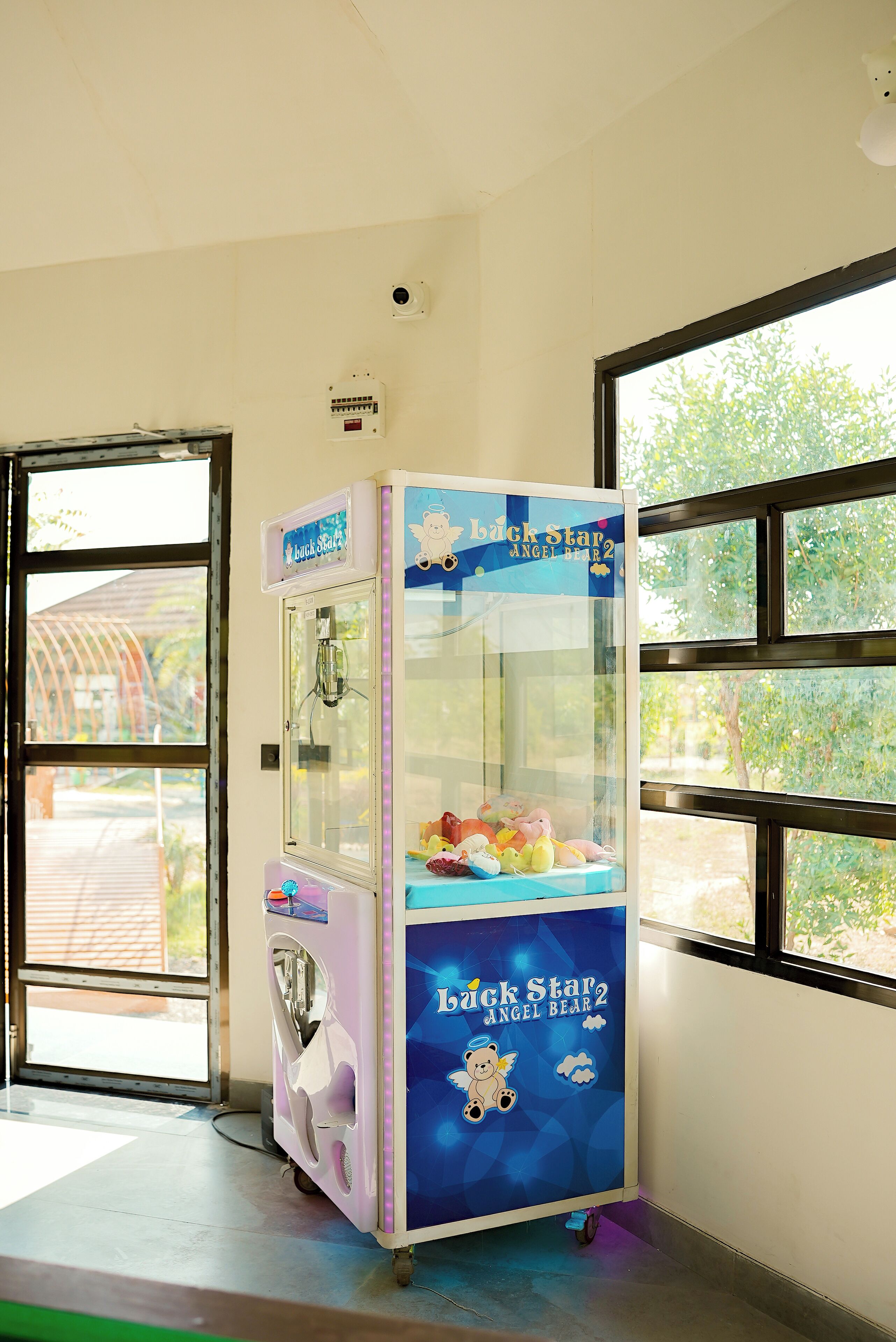 A claw machine in a room with large windows and a door leading outside.