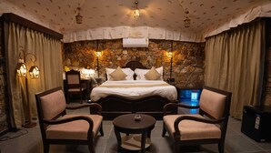 Une chambre d’hôtel avec un mur en pierre, un grand lit avec plusieurs oreillers, deux fauteuils, une petite table et un radiateur.