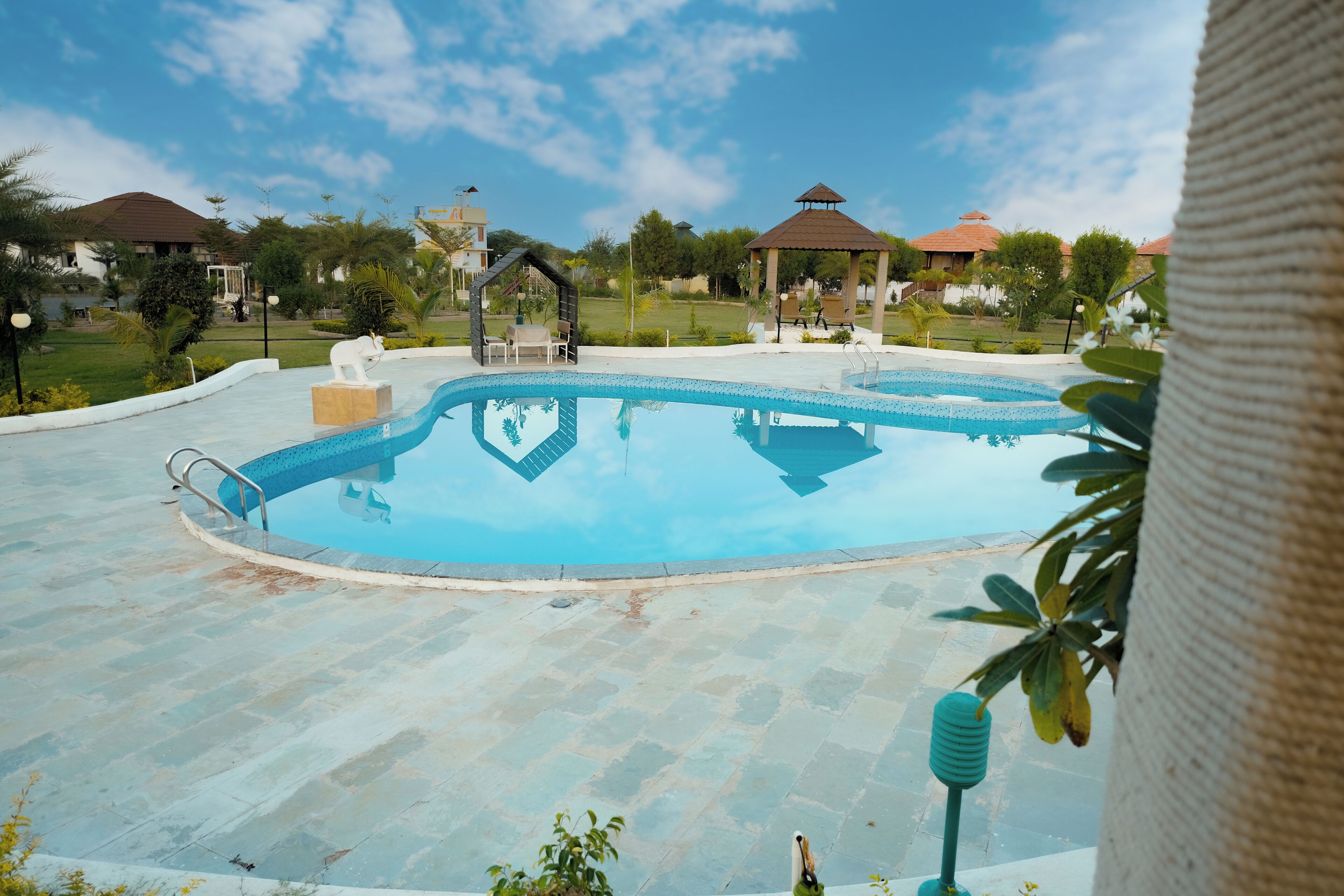 A swimming pool with a gazebo and lounge chairs, surrounded by greenery and buildings.