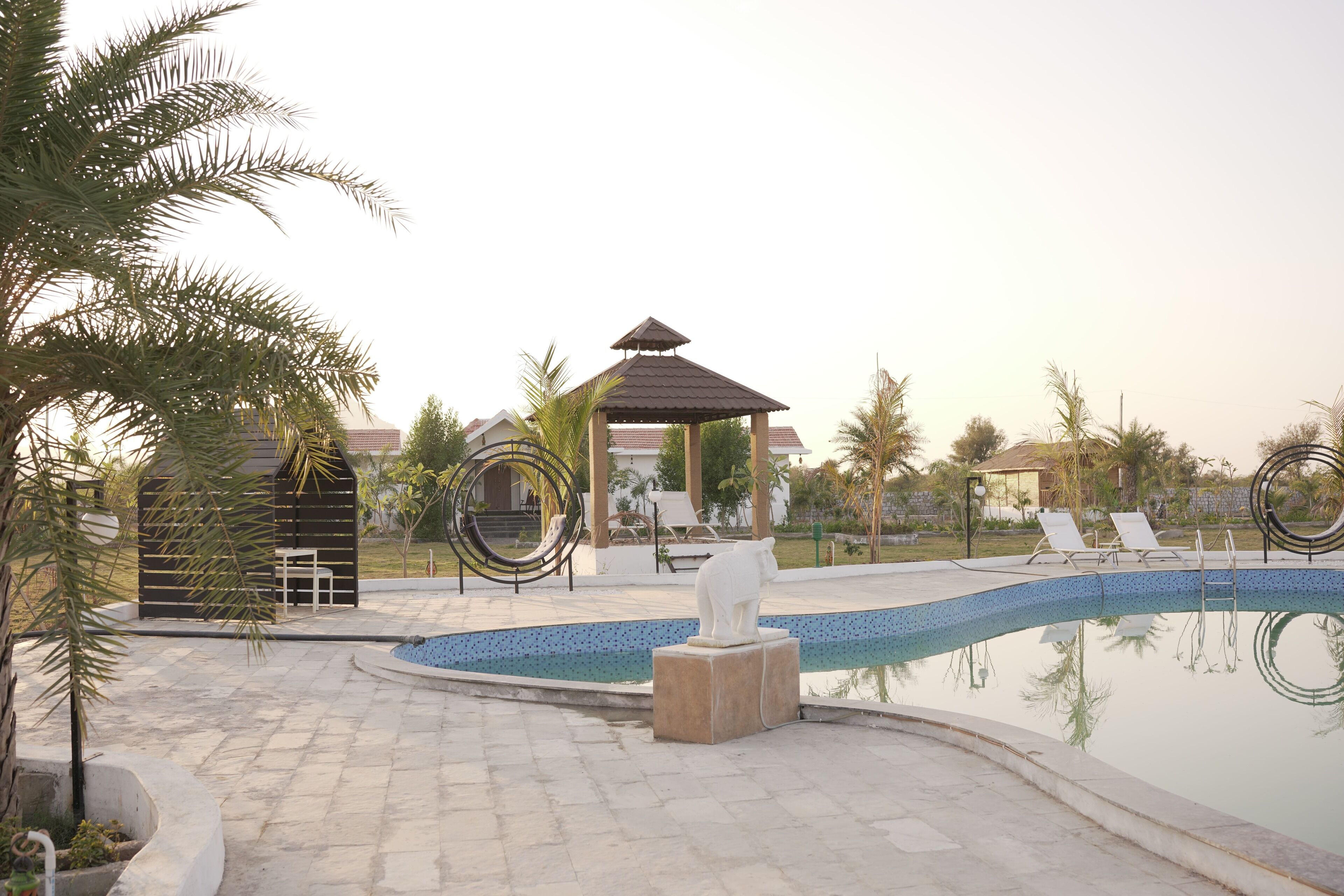 Un espace piscine comprenant des chaises longues, un kiosque et des palmiers.