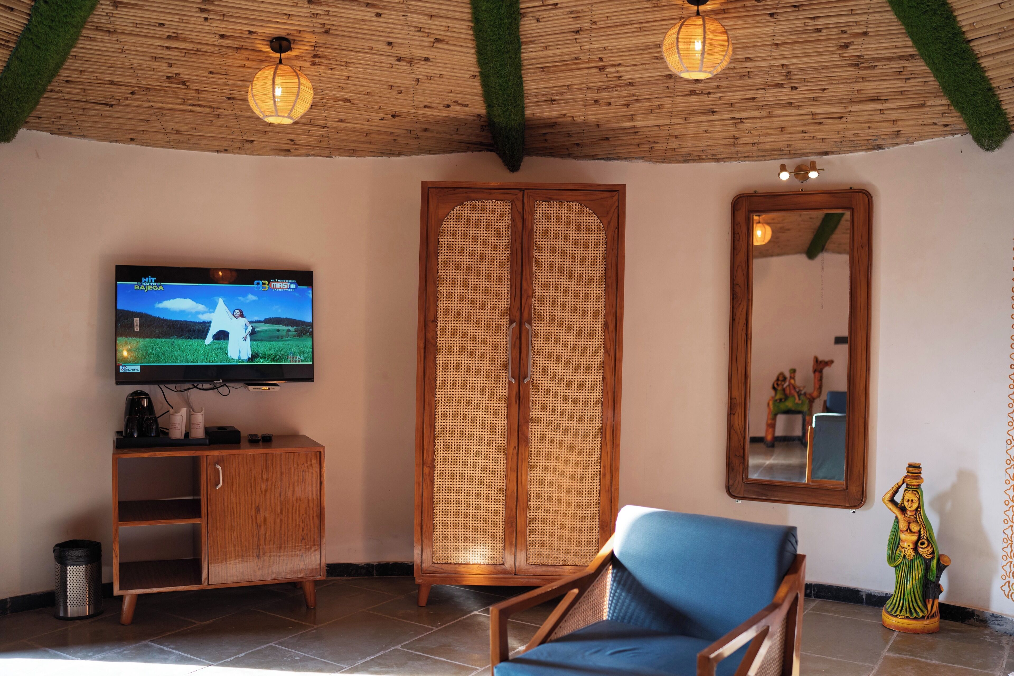 A room with a television, wooden furniture, a mirror, and a statue.