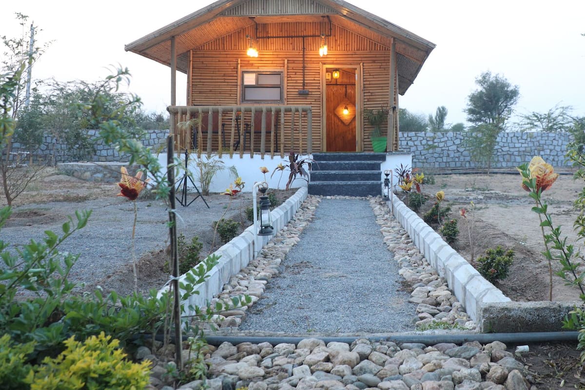 A wooden cabin with a porch, a gravel pathway, and a stone wall in the background.
