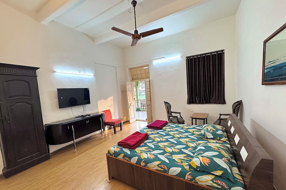 Quarto com cama, escrivaninha, cadeira, televisão e ventoinha no teto.