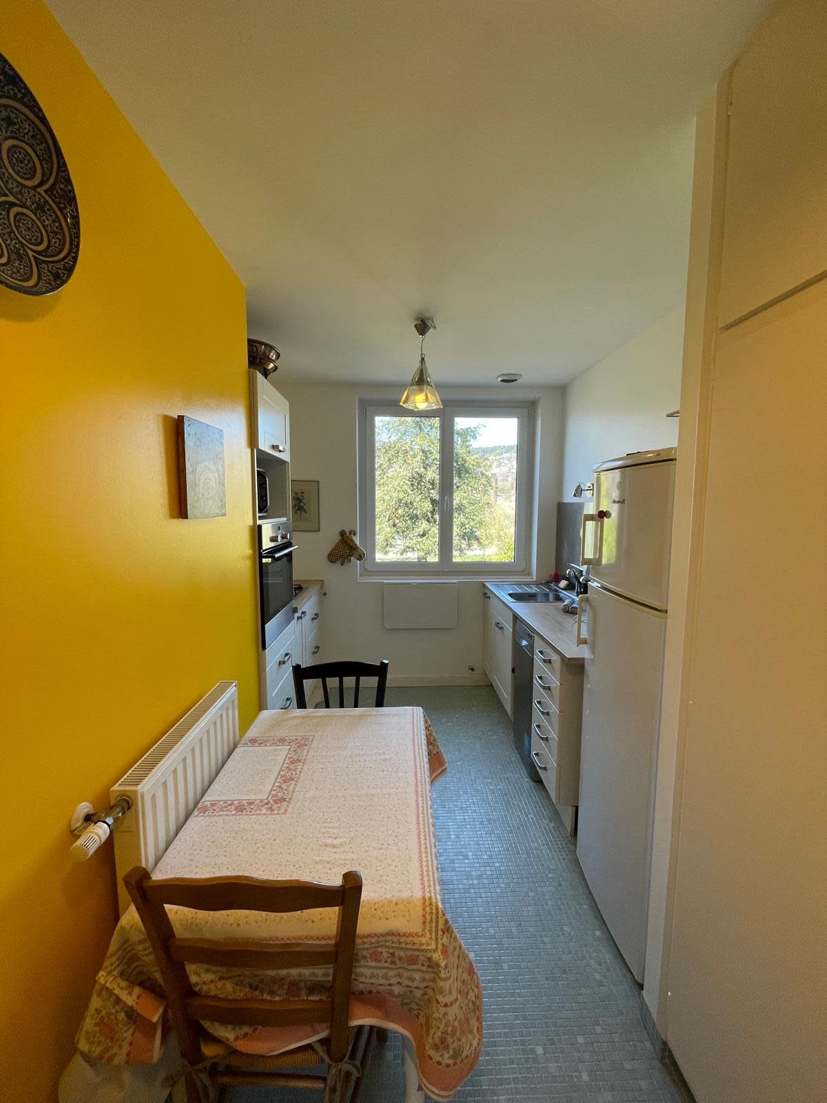 A compact kitchen with a dining table, chairs, a window, and a radiator.