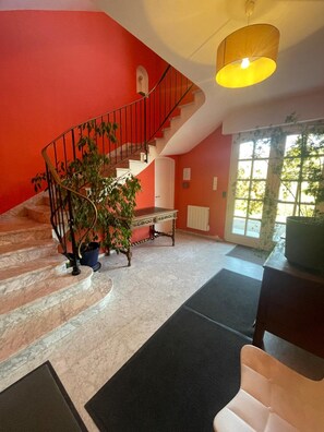 Una escalera con pared roja, barandal negro y una planta en maceta.