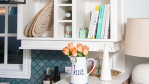 Un mueble blanco con estantes que contienen objetos decorativos, libros y un florero con flores.