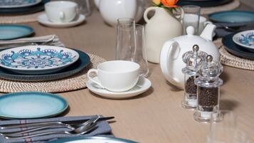 Una mesa dispuesta con platos azules y blancos, una tetera blanca, una taza blanca, un vaso transparente y un salero y pimentero.
