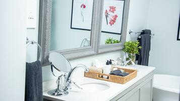 Une salle de bain moderne avec un lavabo blanc, un grand miroir et des œuvres d’art florales encadrées accrochées au mur.