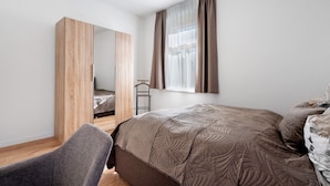 A bedroom with a bed, a chair, a wardrobe, and a window with curtains. - Apartment '2' with Private Terrace, Shared Garden and Wi-Fi (Rathmannsdorf)