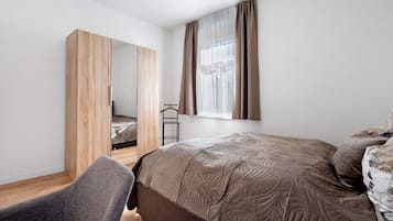 A bedroom with a bed, a chair, a wardrobe, and a window with curtains.