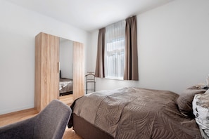 A bedroom with a bed, a chair, a wardrobe, and a window with curtains.