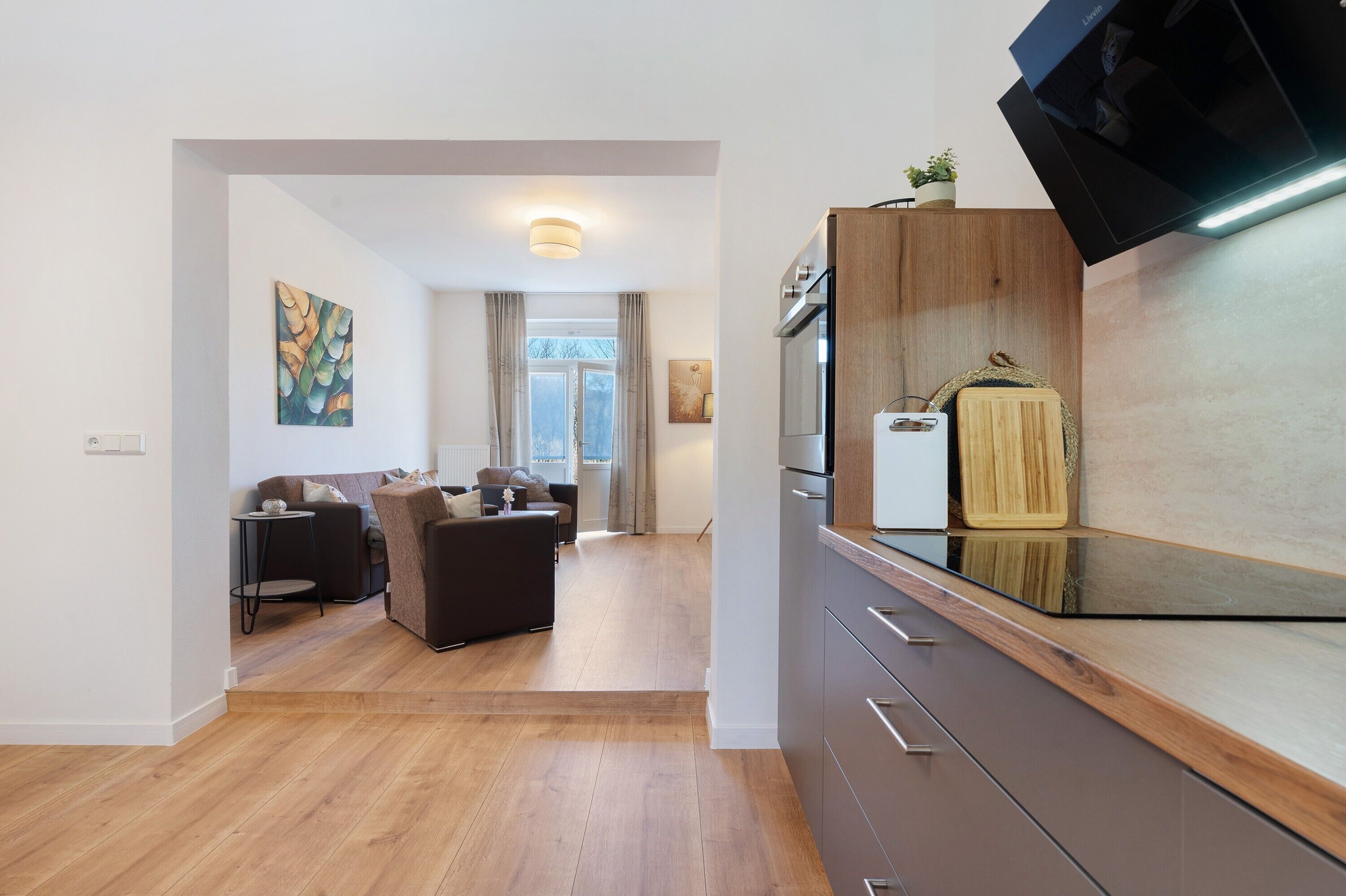 Eine moderne Küche mit Einbauofen, einer Holzausziehtafel und einem kleinen Topf mit Pflanze auf der Arbeitsfläche.
