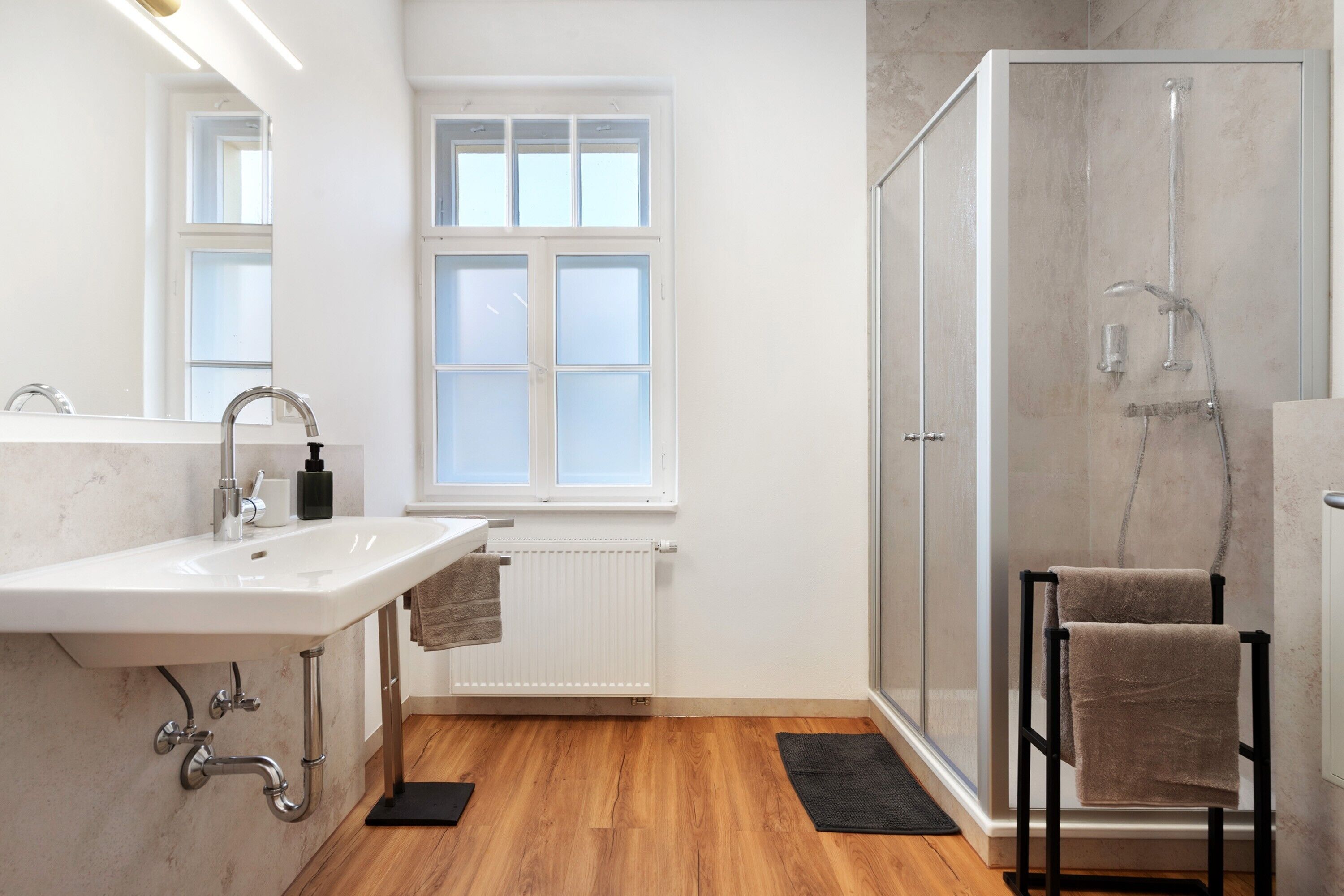 Ein Badezimmer mit Waschbecken, Spiegel, Fenster, Dusche und Handtuchhalter.
