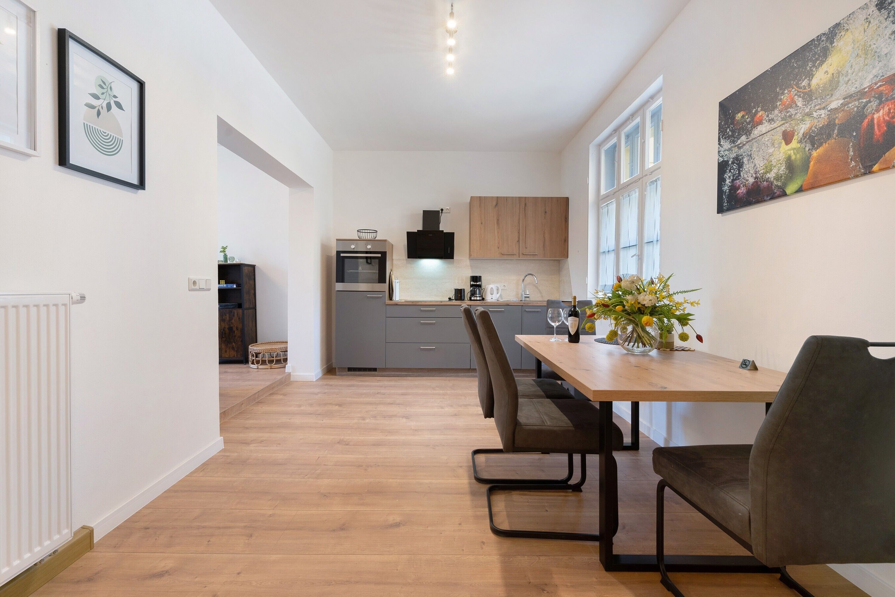 Eine moderne Küche mit Holzausstattung, einem Esstisch mit Stühlen und einer Blumenvase.