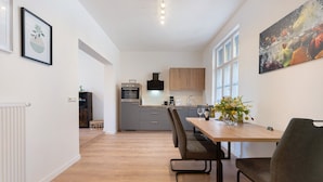 A modern kitchen with wooden cabinets, a dining table with chairs, and a vase with flowers. - Apartment '2' with Private Terrace, Shared Garden and Wi-Fi (Rathmannsdorf)