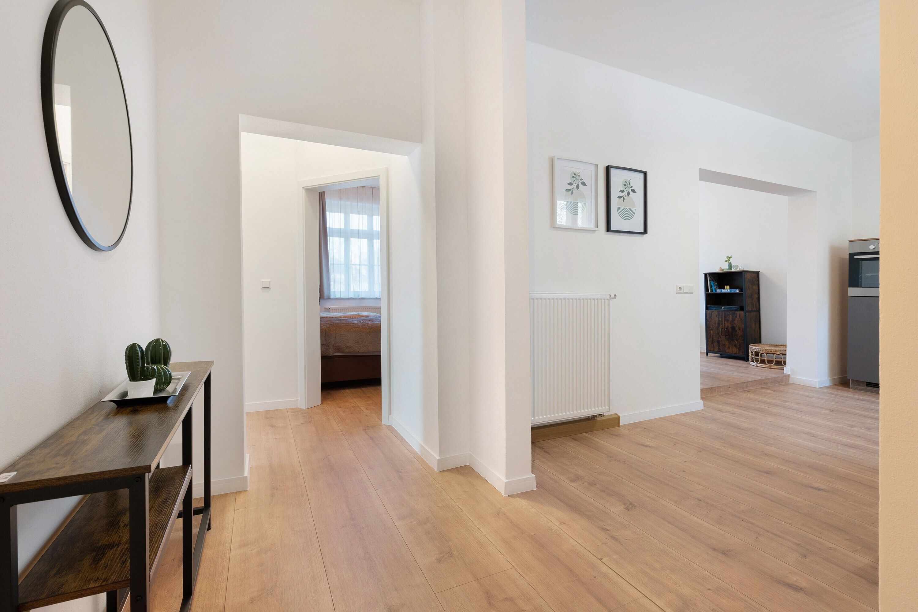 Ein geräumiges Zimmer mit Holzboden, einem dunklen Holztisch, einem Spiegel und einem Durchgang zu einem anderen Raum.