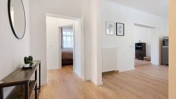 Ein geräumiges Zimmer mit Holzboden, einem dunklen Holztisch, einem Spiegel und einem Durchgang zu einem anderen Raum.