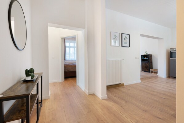 A spacious room with a wooden floor, a dark wooden table, a mirror, and a doorway leading to another room.