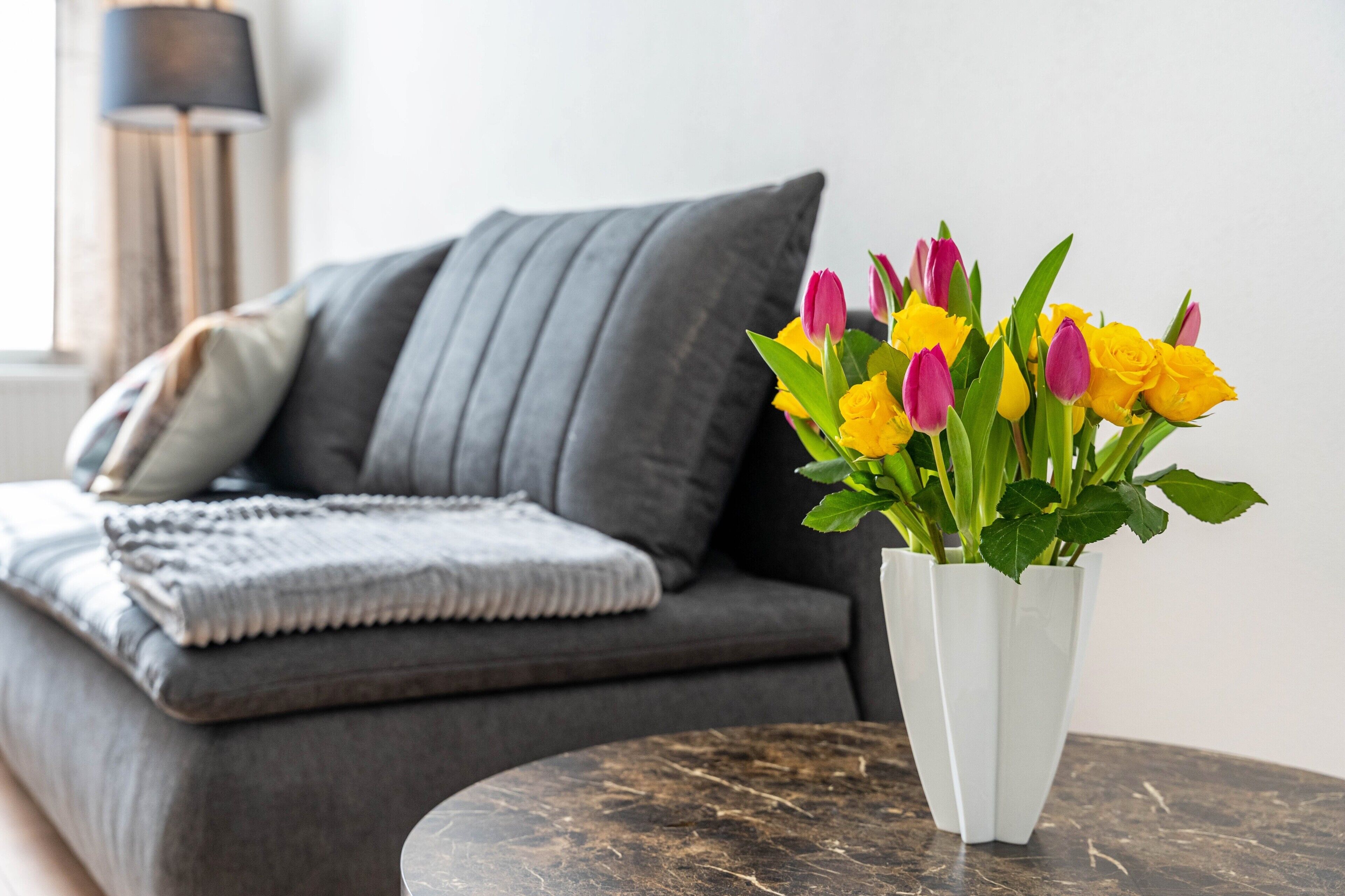 Ein modernes Wohnzimmer mit einem grauen Sofa, einer weißen Vase mit Blumen und einem Marmortisch.