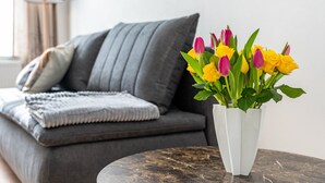 Een moderne woonkamer met een grijze bank, een witte vaas met bloemen en een marmeren salontafel.