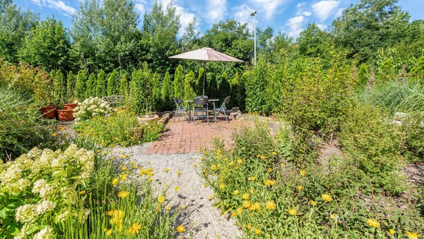 Een terras met een tafel en stoelen, omringd door verschillende planten en bloemen.