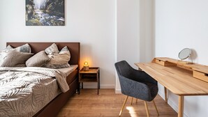 Een slaapkamer met een bed, nachtkastje, lamp, stoel en bureau met spiegel.