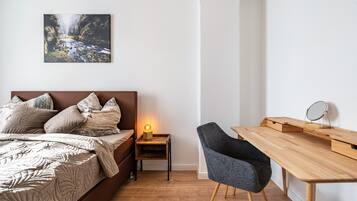 Ein Schlafzimmer mit Bett, Nachttisch, Lampe, Sessel und Schreibtisch mit Spiegel.