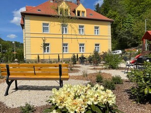 A yellow building with multiple windows, a bench, and a garden area with flowers. - Apartment '4' with Shared Garden and Wi-Fi (Rathmannsdorf)