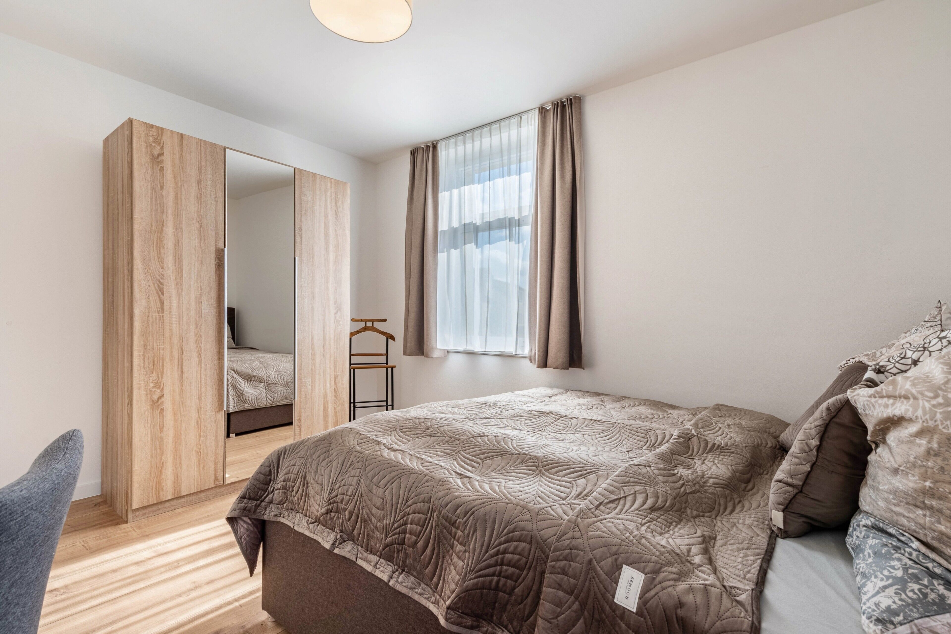 Ein Schlafzimmer mit Bett, Kleiderschrank, Spiegel und einem Fenster mit Vorhängen.