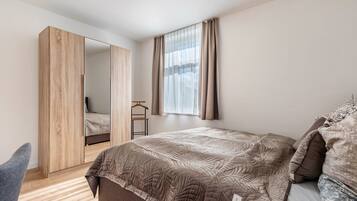 Ein Schlafzimmer mit Bett, Kleiderschrank, Spiegel und einem Fenster mit Vorhängen.