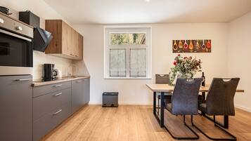 Eine moderne Küche mit grauen Schränken, einem schwarzen Backofen und einem Essbereich mit Tisch und Stühlen.