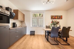 Een moderne keuken met grijze kastjes, een zwarte oven en een eethoek met een tafel en stoelen.