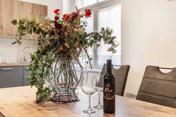 Een eettafel met een wijnfles, twee wijnglazen en een bloemstuk.