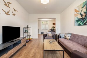 A modern living room with a flat-screen TV, a sofa, a coffee table, and a bookshelf. - Apartment '4' with Shared Garden and Wi-Fi (Rathmannsdorf)