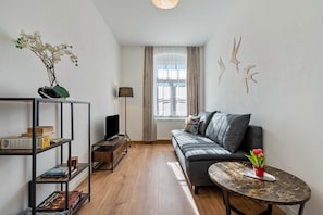 Ein modernes Wohnzimmer mit einer Couch, einem kleinen Tisch, einem Bücherregal und einem Fenster mit Vorhängen.