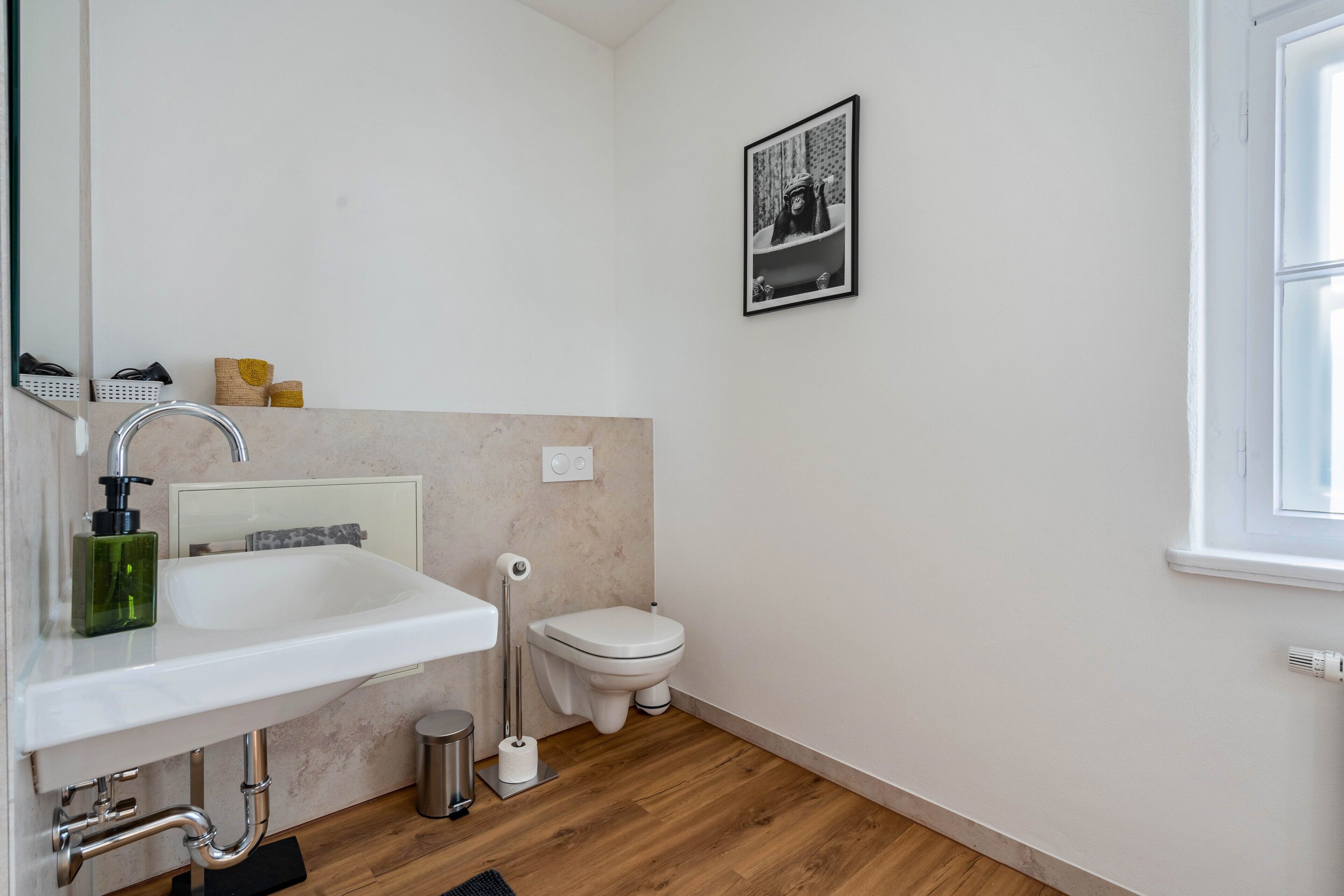 Ein modernes Badezimmer mit einem weißen Waschbecken, einer Toilette und einem gerahmten Bild an der Wand.