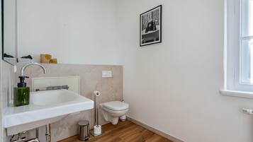 Ein modernes Badezimmer mit einem weißen Waschbecken, einer Toilette und einem gerahmten Bild an der Wand.