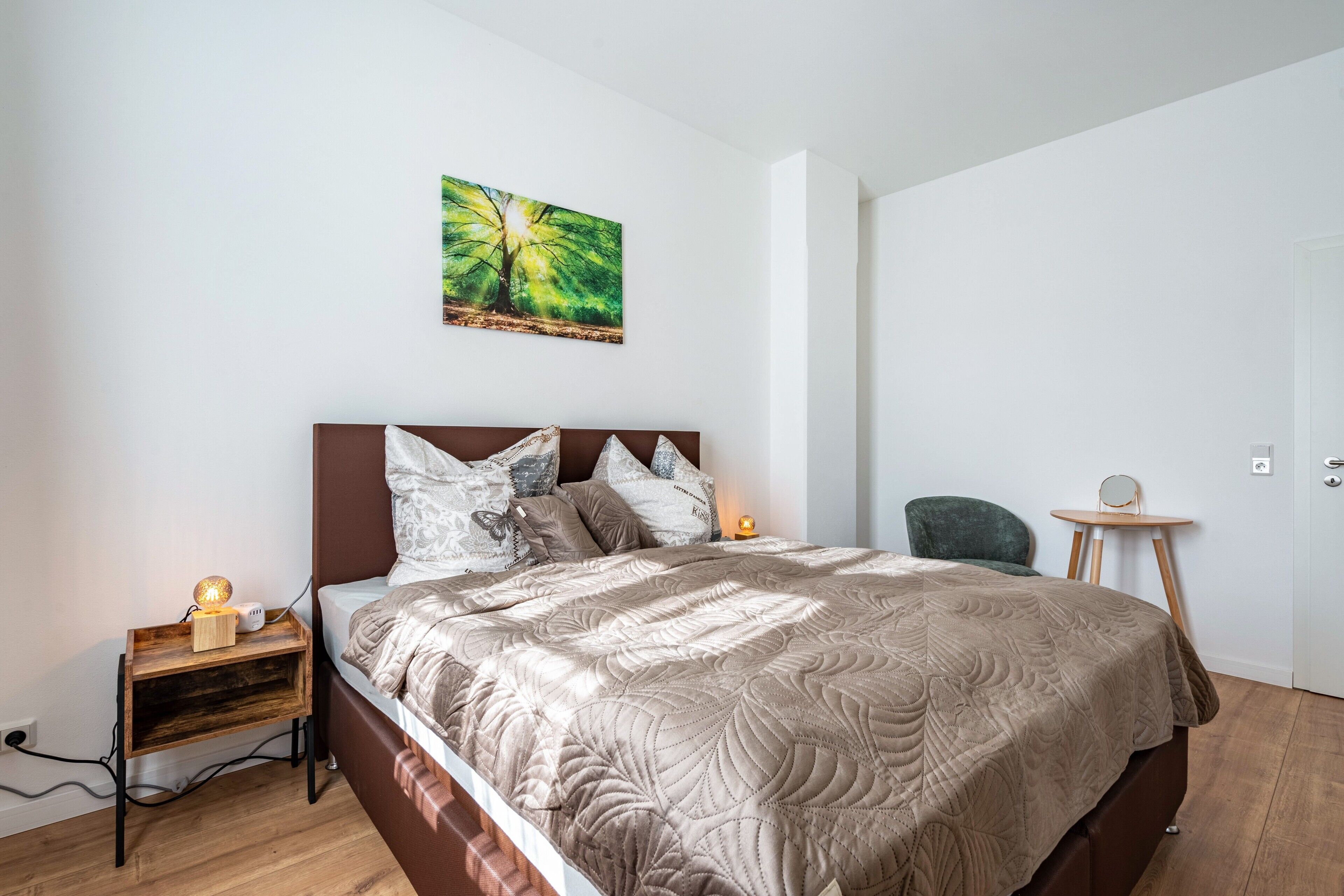 Ein Schlafzimmer mit Bett, Nachttisch, Lampe, Stuhl und einem Gemälde an der Wand.
