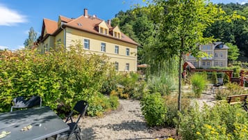 Ein zweistöckiges Gebäude mit rotem Ziegeldach, umgeben von üppigem Grün und einem Kiesweg.