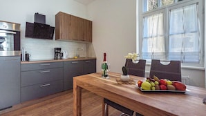 A modern kitchen with grey cabinets, a wooden dining table, and a fruit platter.