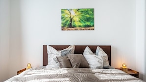 A bed with a quilted pattern, a painting of a tree, and two bedside lamps.