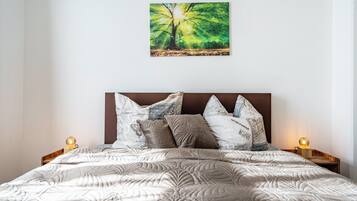 Ein Bett mit einer gesteppten Musterung, ein Baumgemälde und zwei Nachttischlampen.